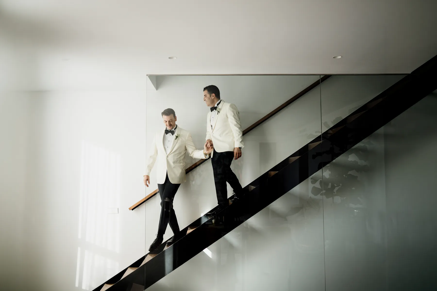 Los novios bajan la escalera de la mano, de esmoquin blanco