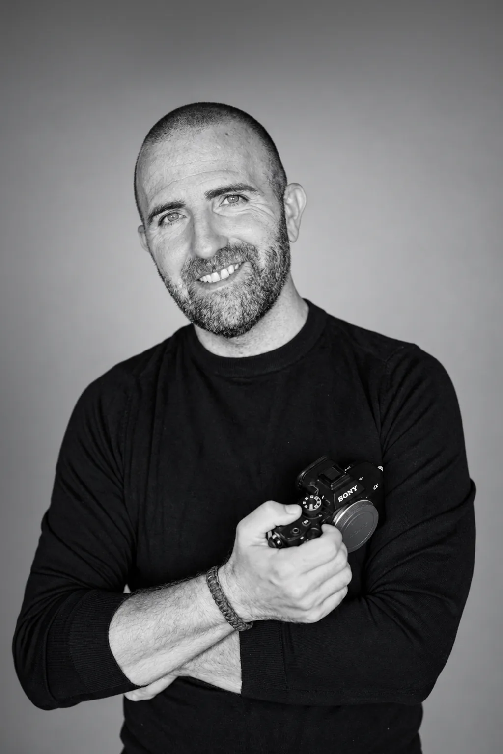 Retrato en blanco y negro de Juanfra García sonriendo, con su cámara en la mano