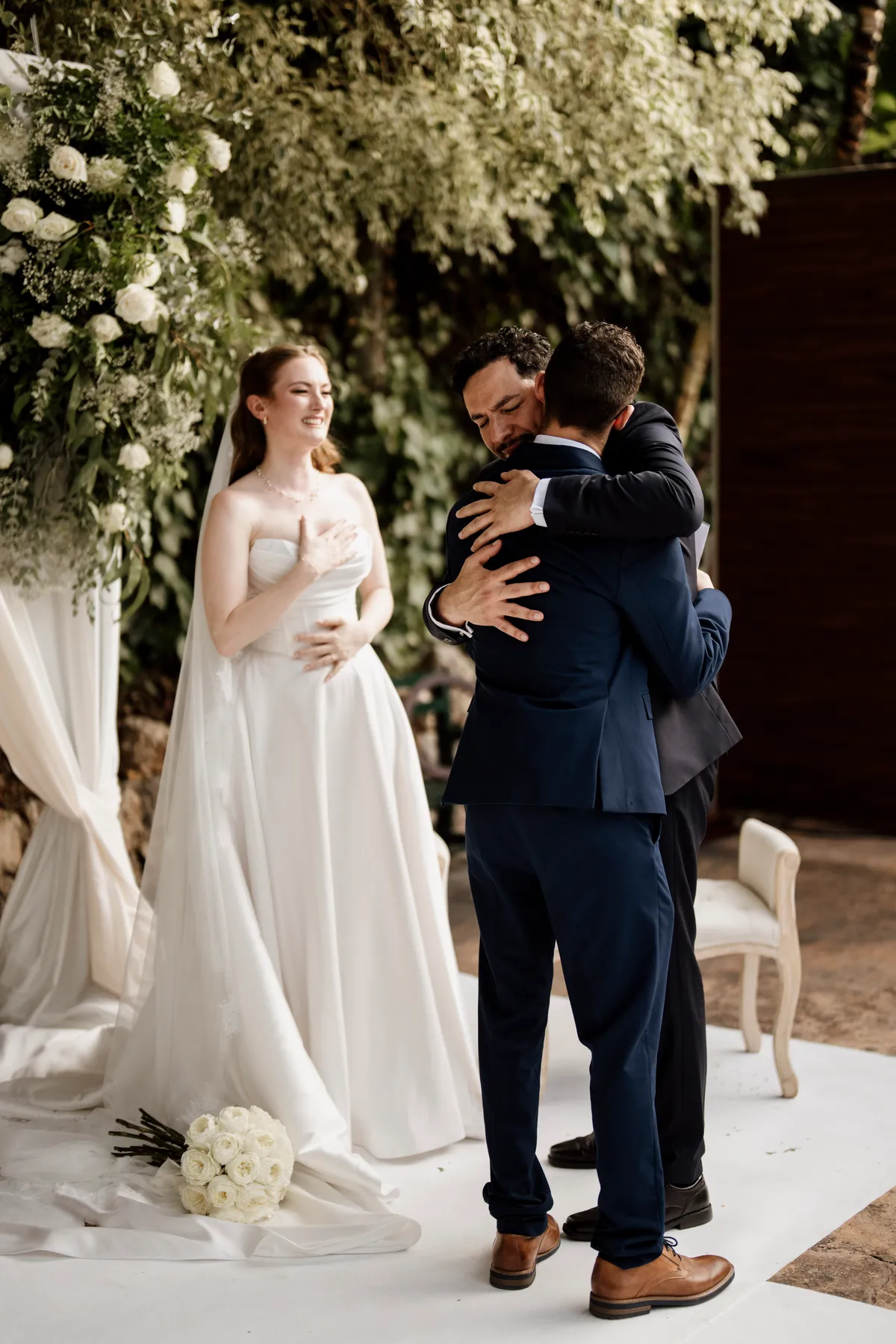 La novia sonríe emocionada ante un abrazo junto al arco de flores